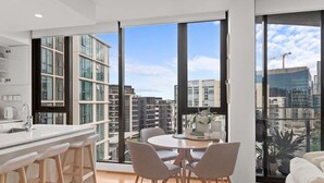A modern kitchen with a large island, bar stools, and a dining area with a round table and chairs. - Modern Panoramic Luxury in Fortitude Valley (Brisbane)