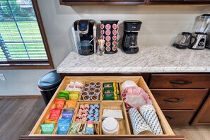 Eine Küche mit Marmorarbeitsplatte, Kaffeemaschinen und einer Schublade voller Lebensmittel.