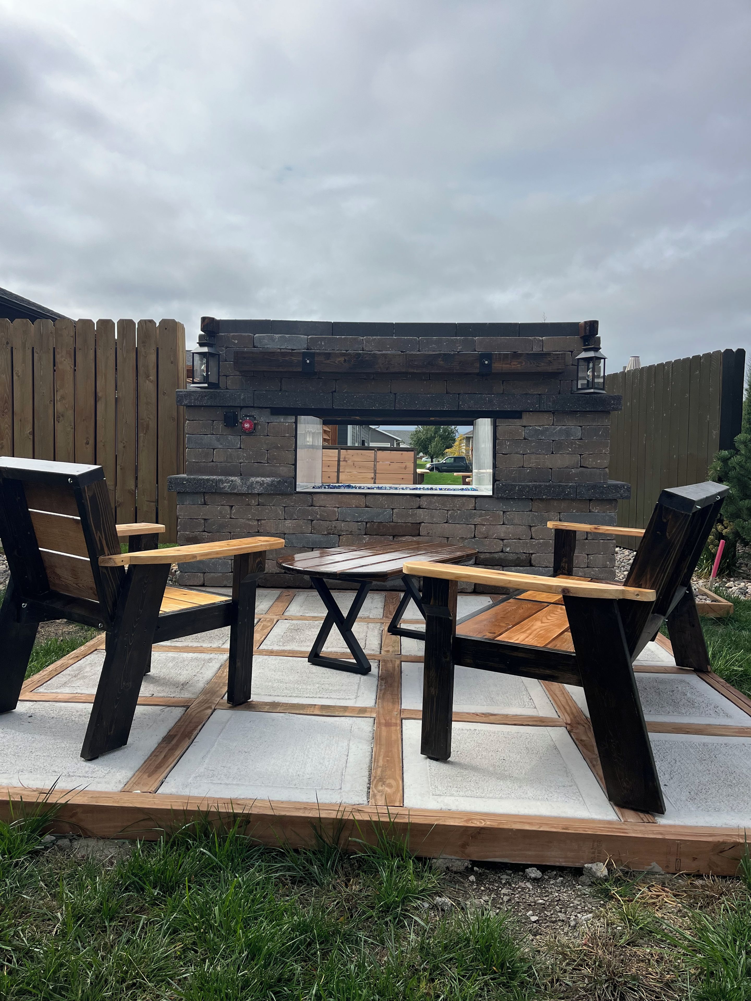 Un patio al aire libre con chimenea de piedra, sillas de madera y una mesa.