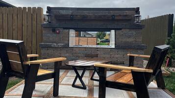 Un patio al aire libre con chimenea de piedra, sillas de madera y una mesa.