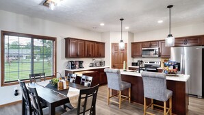 A modern kitchen with wooden cabinets, a central island with bar stools, and a large window overlooking a yard.