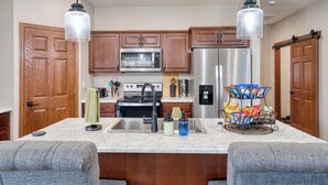 A kitchen with wooden cabinets, stainless steel appliances, a marble countertop, and a central island with a sink.