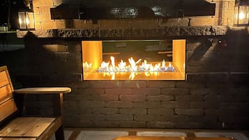 Un área de estar al aire libre con chimenea de piedra, bancos y una mesa.