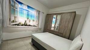 A bedroom with a bed, a wardrobe, a window with curtains, and a view of palm trees. - Apartment 2 Blocks from Guilhermina Beach-Praia Grande SP! Near Boqueirão (Praia Grande)