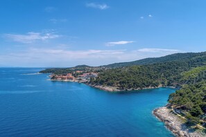 A coastal town with buildings along the shoreline, surrounded by hills and a clear blue sea.