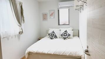 A bedroom with a bed, a window, an air conditioning unit, and a door.