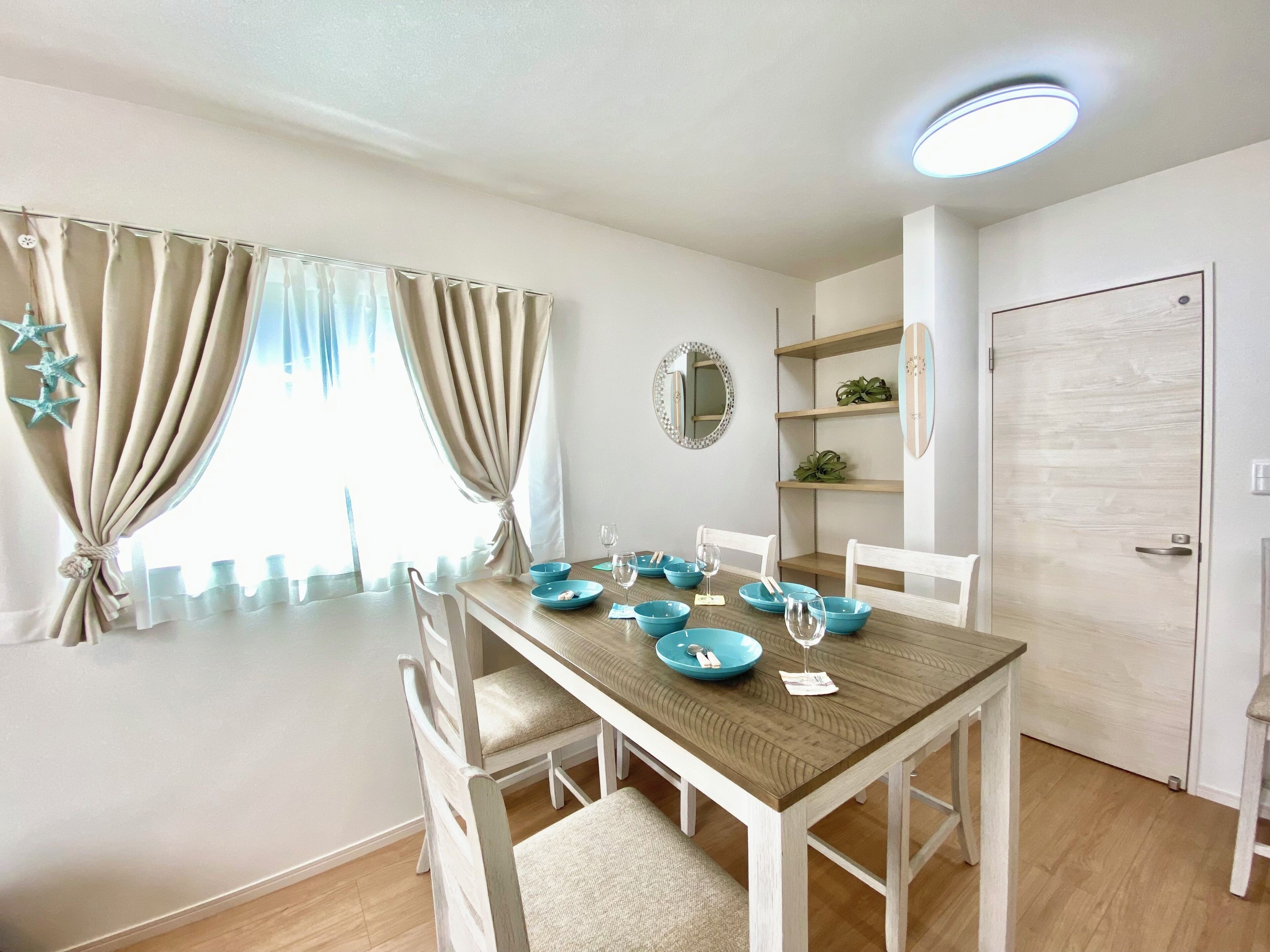 A dining area with a wooden table, white chairs, blue bowls, and a mirror on the wall.