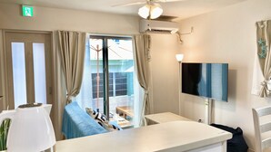 A hotel room with a ceiling fan, air conditioning unit, a TV mounted on the wall, a coffee maker on the counter, and a sliding glass door leading to a balcony. - New Onna | Cozy BBQ terrace, 8-min beach, snorkeling, SUP, sleeps 7, parking (恩納村)