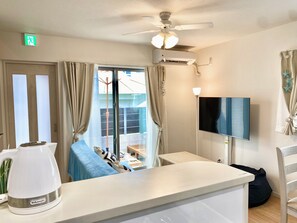 A hotel room with a ceiling fan, air conditioning unit, a TV mounted on the wall, a coffee maker on the counter, and a sliding glass door leading to a balcony.