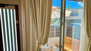 A room with a large sliding glass door, a wooden table with blue plates, and a view of a residential area. - New Onna | Cozy BBQ terrace, 8-min beach, snorkeling, SUP, sleeps 7, parking (恩納村)