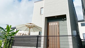 A modern building with a flat roof, a small window, and a door with a vertical wooden panel. - New Onna | Cozy BBQ terrace, 8-min beach, snorkeling, SUP, sleeps 7, parking (恩納村)