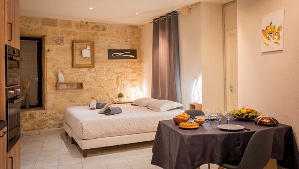 Ein gemütliches Zimmer mit Steinwand, einem Bett mit beigefarbener Bettdecke, einem Esstisch gedeckt mit Tellern, Gläsern und einer Obstschale.