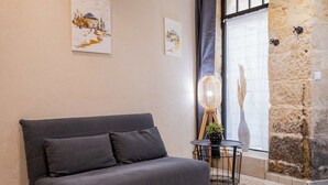 Ein modernes Wohnzimmer mit einem grauen Sofa, einem kleinen Beistelltisch mit Lampe und einer Steinwand.