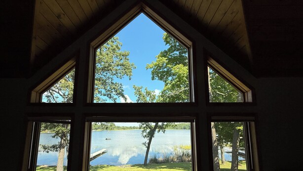 Ein Zimmer mit großem Fenster und Blick auf einen See und eine Wiese.