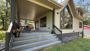 Ein Haus mit überdachter Veranda, Sitzgelegenheiten im Freien und einer Steintreppe, die zum Eingang führt.