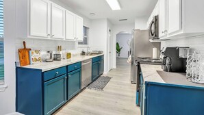 A modern kitchen with white cabinets, blue accents, a stainless steel refrigerator, and a coffee machine.