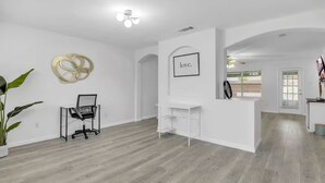 A spacious room with a wooden floor, a desk, a chair, and a potted plant.