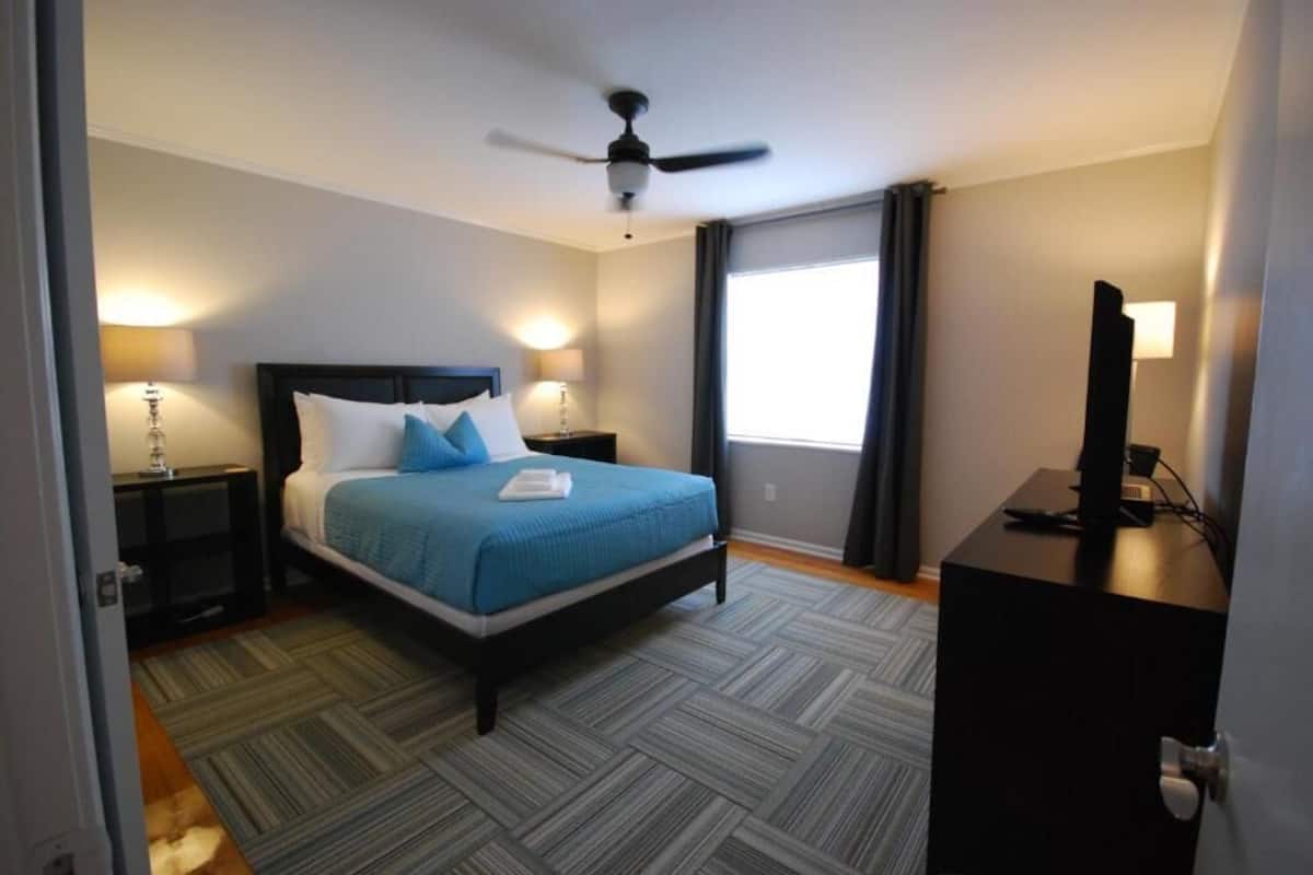 A hotel room with a bed, a desk, a ceiling fan, and a window.
