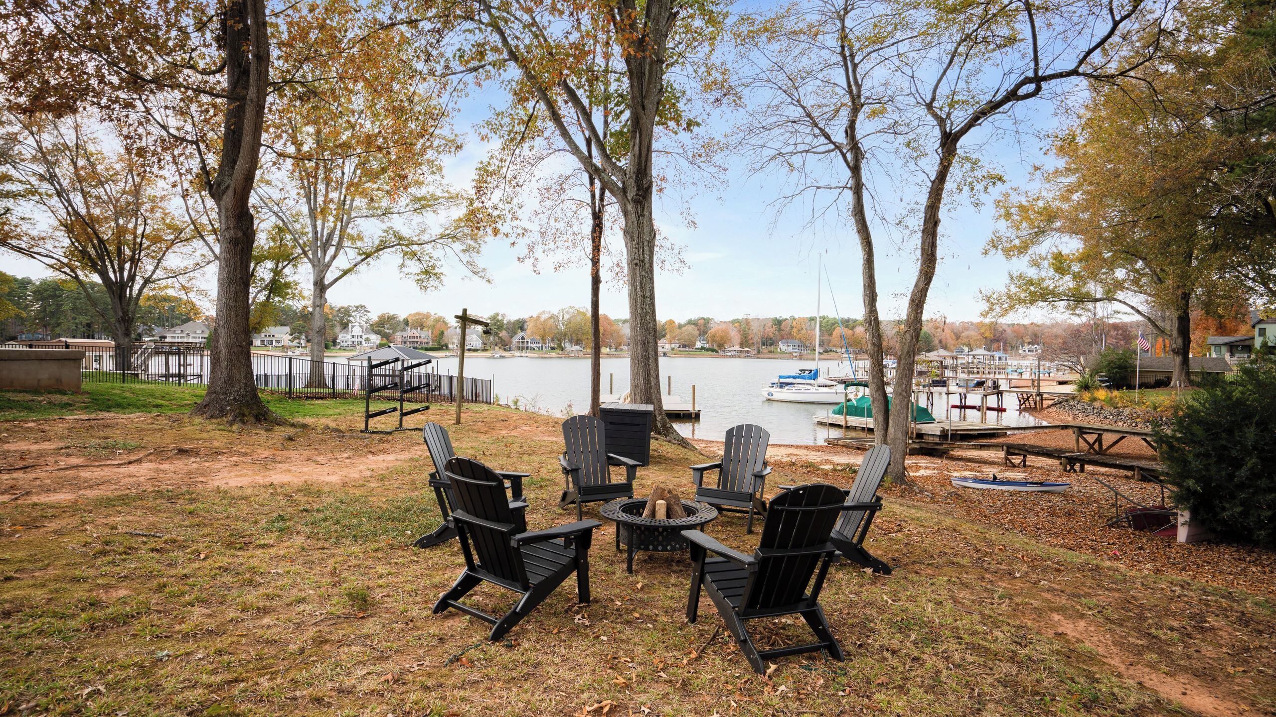 A lakeside outdoor seating area with Adirondack chairs and a fire pit.