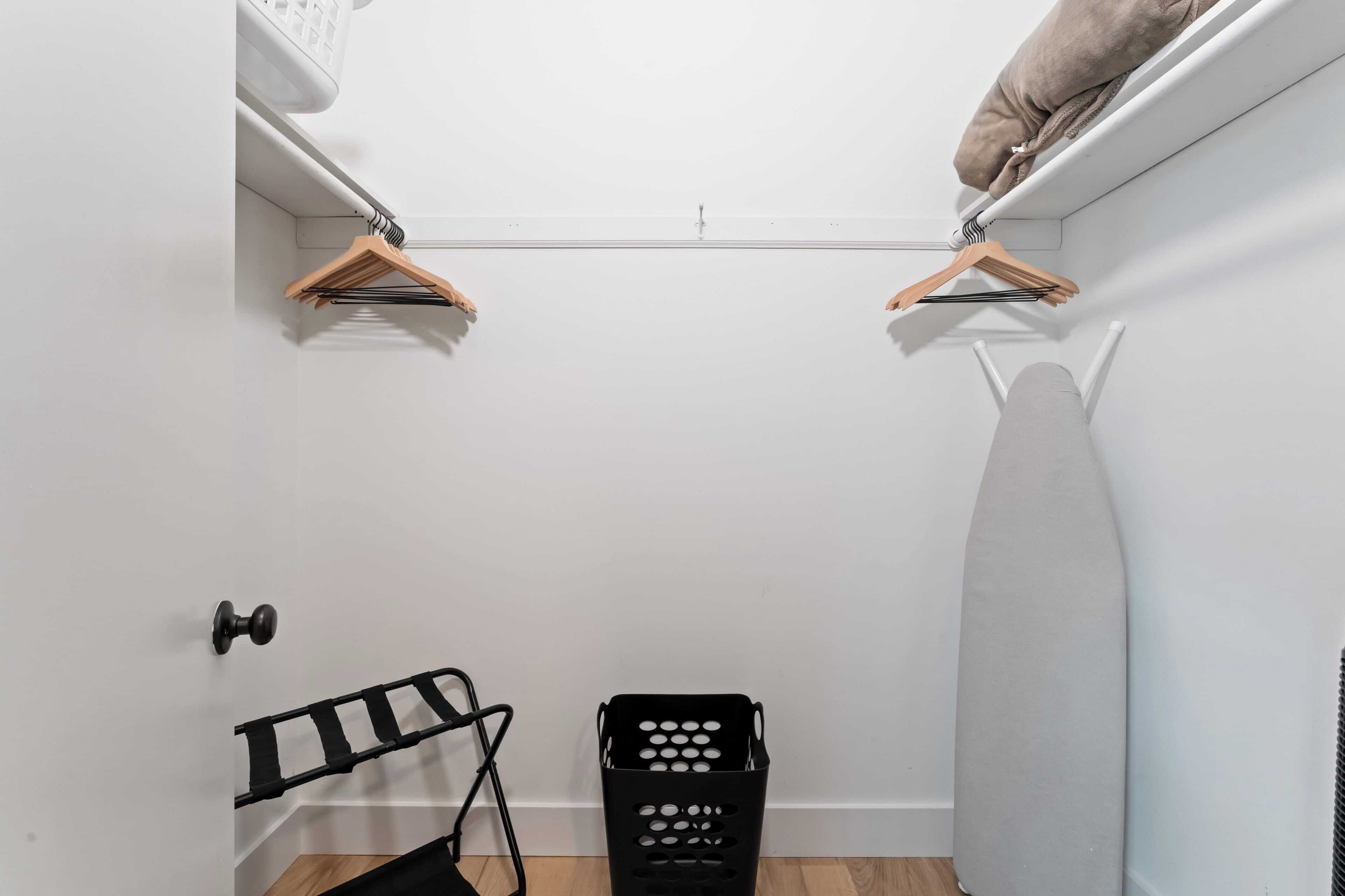 A small laundry room with a drying rack, ironing board, and a laundry basket.