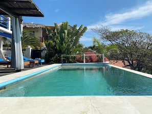 A swimming pool with lounge chairs and a thatched-roof building in the background.