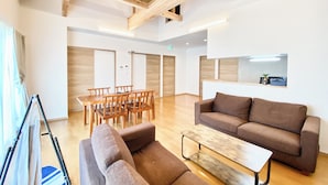 A spacious room with a wooden ceiling, a sofa, a coffee table, a dining table with chairs, and a reception desk.