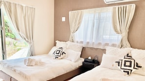 A double bed with white bedding, a bedside table with a lamp, and a window with curtains.