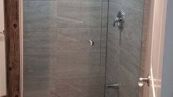A walk-in shower with a glass door, tiled walls, and a small window.