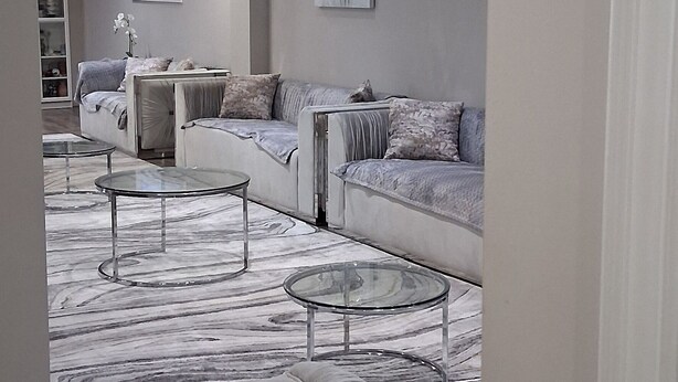 Un salon moderne avec un tapis à motifs de marbre, un canapé et une table basse en verre.