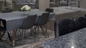 Un espace repas moderne avec un comptoir en marbre, des chaises recouvertes d’un tissu gris et une nappe grise.