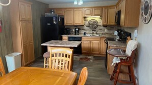 A compact kitchen with wooden cabinets, a refrigerator, a coffee maker, and a dining area with a table and chairs. - Charming 5BR House with Views of the Slopes, Full Kitchen, Patio, and Wifi (Beech Mountain)