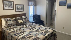 A bedroom with a bed featuring a bear-themed quilt, a chair, and two framed pictures on the wall. - Charming 5BR House with Views of the Slopes, Full Kitchen, Patio, and Wifi (Beech Mountain)