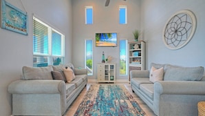 A living room with two grey sofas, a patterned rug, a television, and a decorative wall piece.