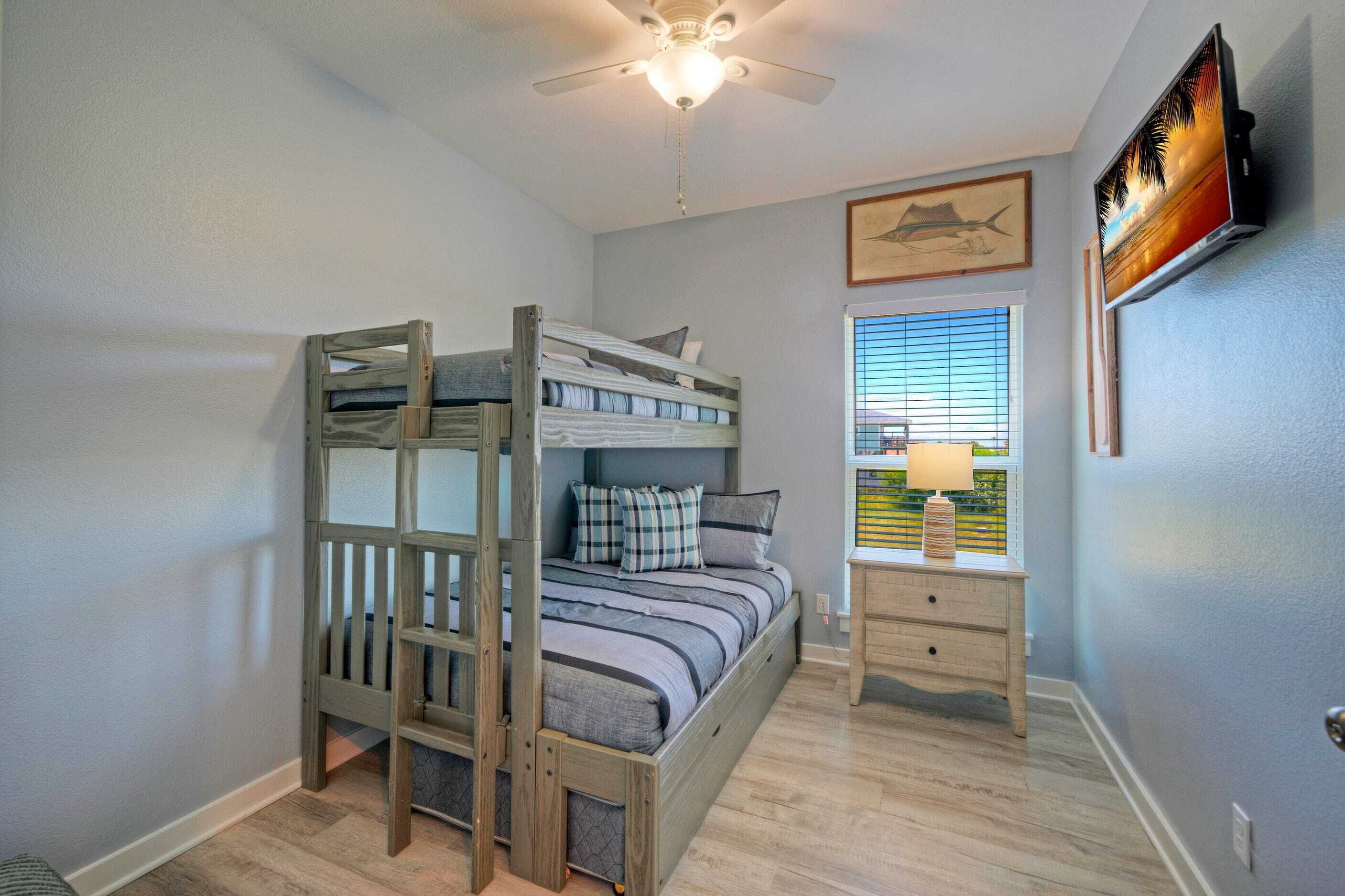 A bunk bed room with a ceiling fan, a window with blinds, a nightstand, and a wall-mounted TV.