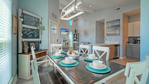A dining area with a wooden table set for four, white chairs, and a chalkboard sign above the door.