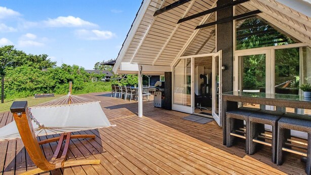 A wooden deck with a hammock, a covered seating area, and a glass door leading to a room.