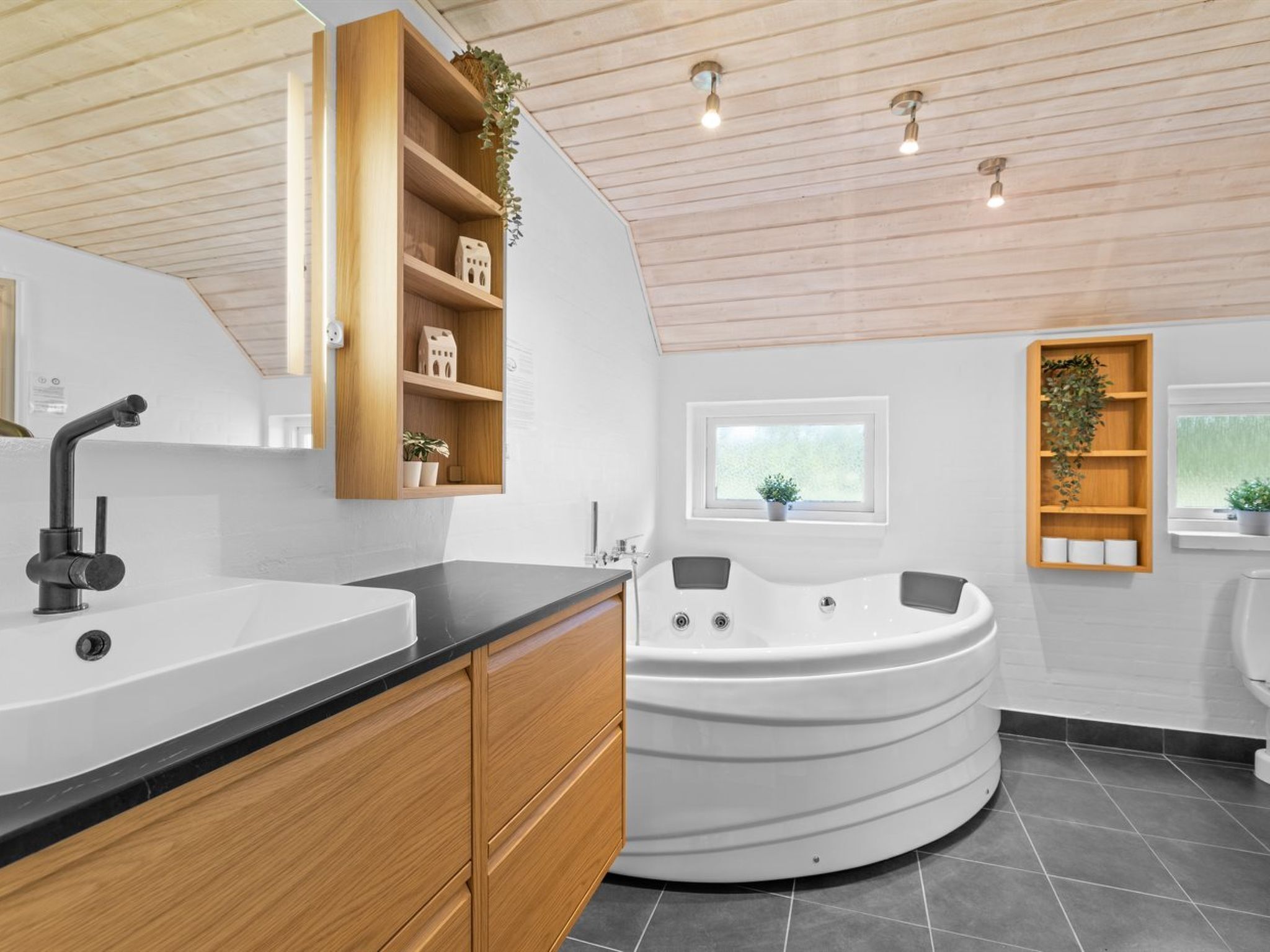 Une salle de bain moderne avec une baignoire sur pieds, des étagères en bois ornées de plantes et une grande fenêtre.