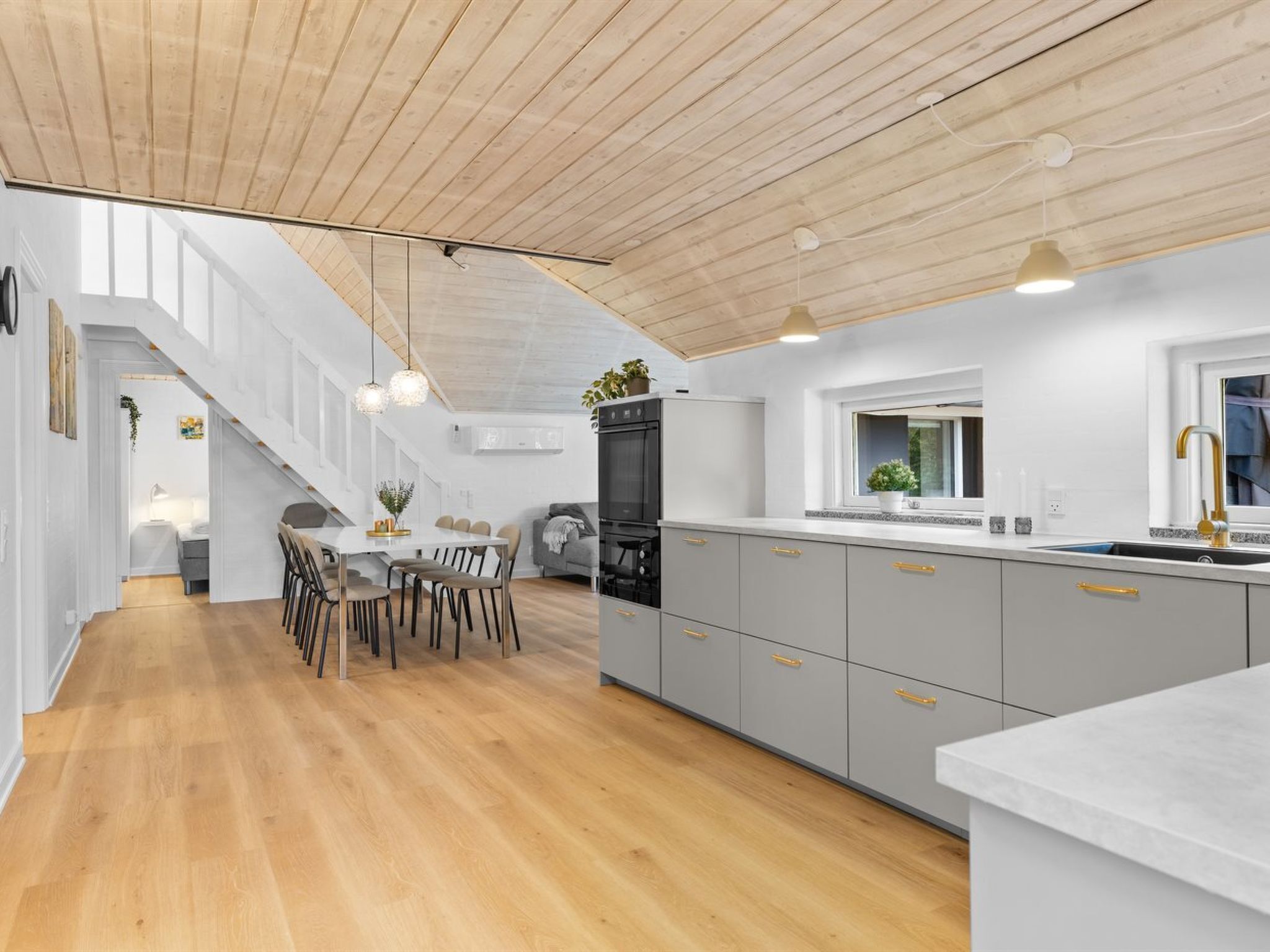 A modern kitchen with grey cabinets, a wooden ceiling, and pendant lighting.