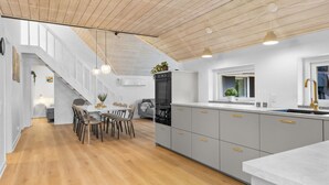 A modern kitchen with grey cabinets, a wooden ceiling, and pendant lighting.