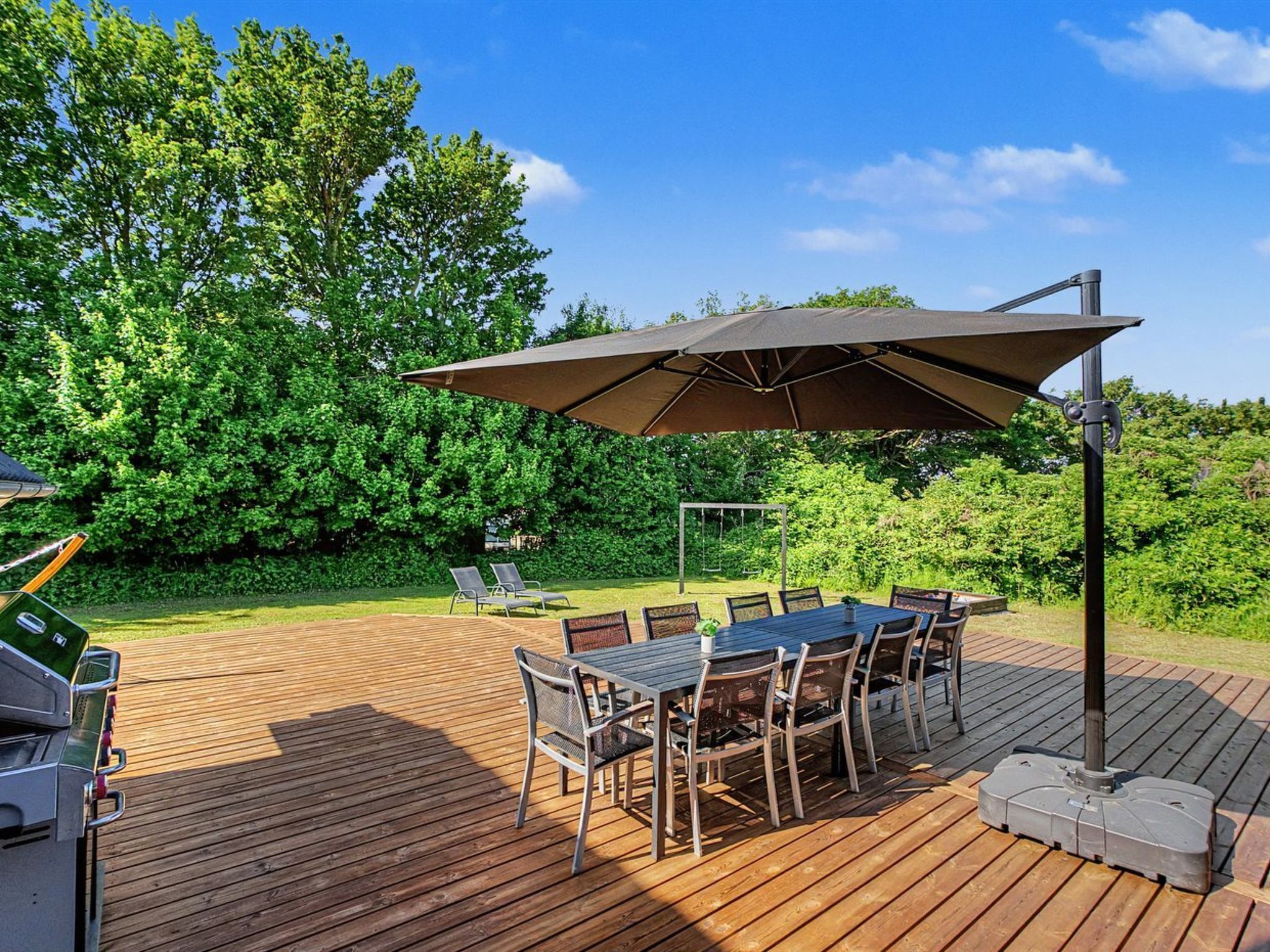 A wooden deck with a table and chairs, a grill, and a swing set.