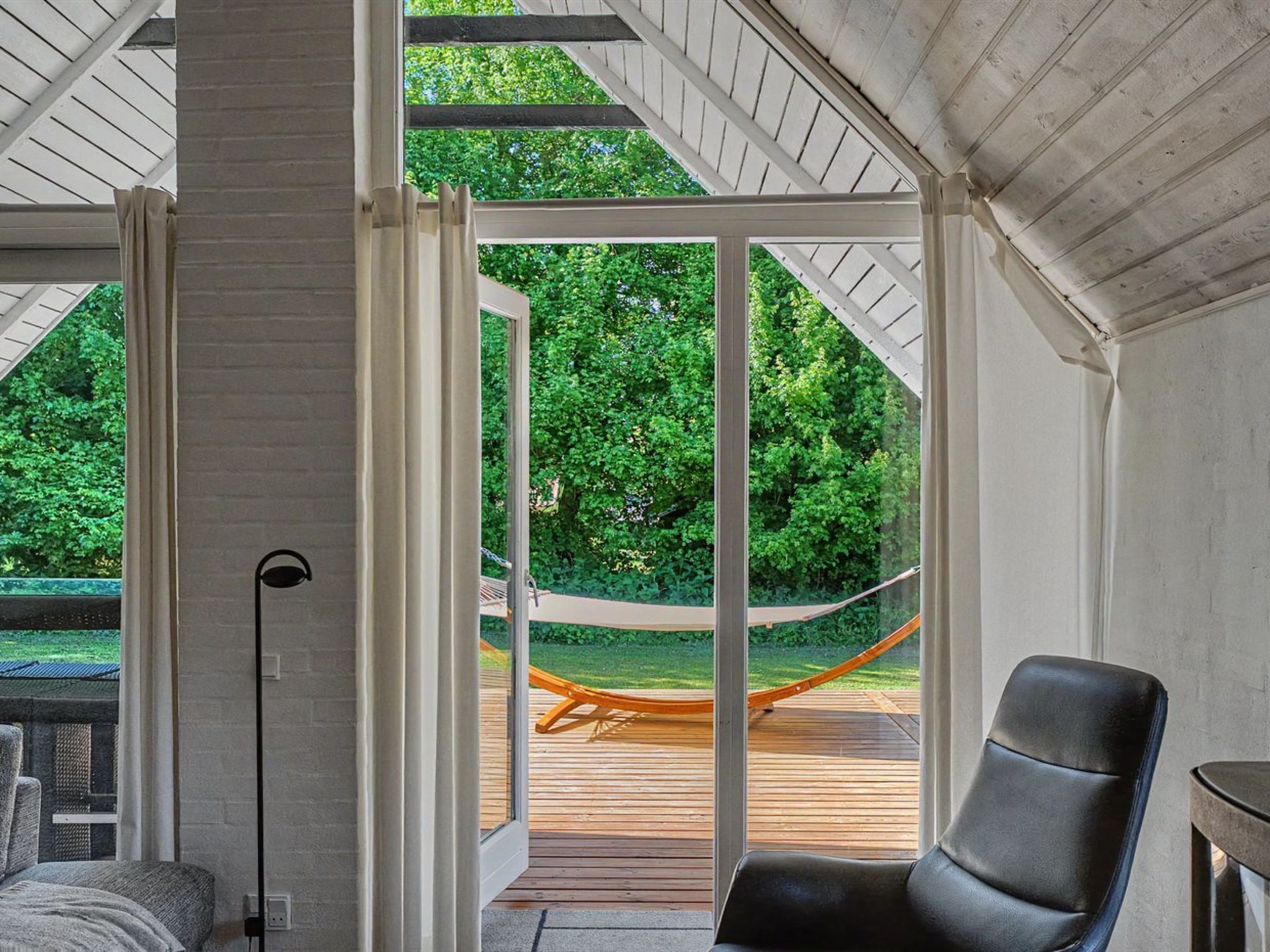 Una habitación con un amplio ventanal corredera que da a una terraza exterior con una hamaca.