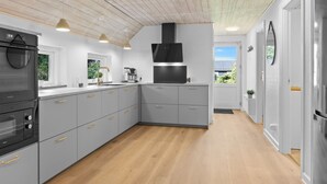 A modern kitchen with grey cabinets, a black range hood, and a wooden ceiling.