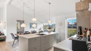 A modern kitchen with a central island, pendant lights, and a view of the outdoors.