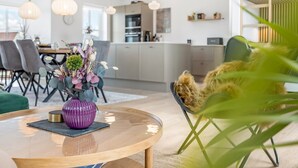 A modern kitchen with white cabinets, a dining area with grey chairs, and a round wooden table with a purple vase.