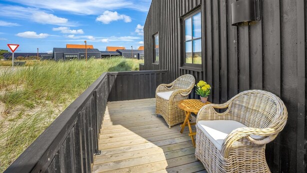 A wooden deck with wicker furniture and a view of the sea.
