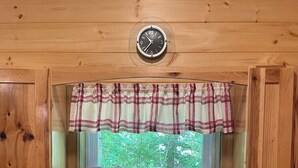 A kitchen with a double sink, wooden cabinets, a window with a plaid valance, and a clock on the wall.