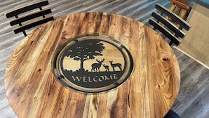 A round wooden table with a central emblem featuring a tree and deer, surrounded by black chairs.