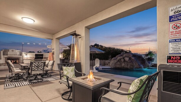 An outdoor patio with a fire feature, seating, a pool, and a grill. - Northstar Zen Resort: Rock Waterslide Pool, Spa, MultiBall Zone & Game Room (Glendale)