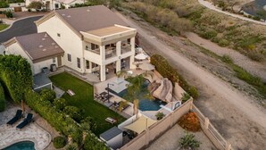 A large two-story house with a swimming pool, outdoor seating, and a view of the surrounding landscape.