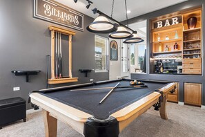 A pool table with a billiards sign, a bar area with shelves, and a window with blinds.